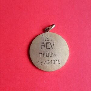 May include: A gold-colored metal medal with the text "HET ACV TROUW 1920-1949" engraved on the front.