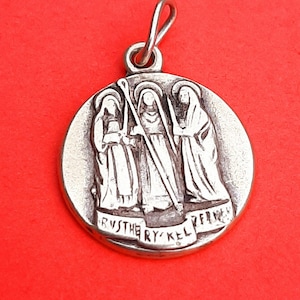 May include: Silver pendant featuring three figures in robes, with a staff and the inscription "RVS THE RY KEL ZFRN" around the edge.