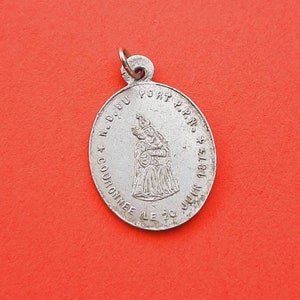May include: Silver pendant with a religious image of a woman holding a baby. The pendant is inscribed with the text "N.D. DU PORT P.P.P.N.S. COURONNEE LE 20 JUIN 1875".