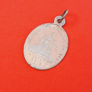 Könnte beinhalten: Silberner ovaler Anhänger mit einer Darstellung einer Kirche und dem Text "SANCTUARIO DE N.S. DO ROSARIO LOURDES 1908".