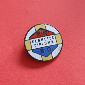 Op de afbeelding: Een ronde, metalen pin met een geel, rood, wit en blauw ontwerp. De pin heeft de tekst "EENHEIDS DIPLOMA B.O." in zwarte letters.