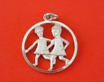 May include: Silver charm pendant featuring the astrological sign Gemini, depicted as two figures facing each other, with a circular cutout design.