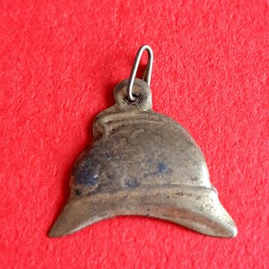 May include: A small, antique, brass-colored pendant shaped like a helmet. The pendant has a loop at the top for attaching to a chain.