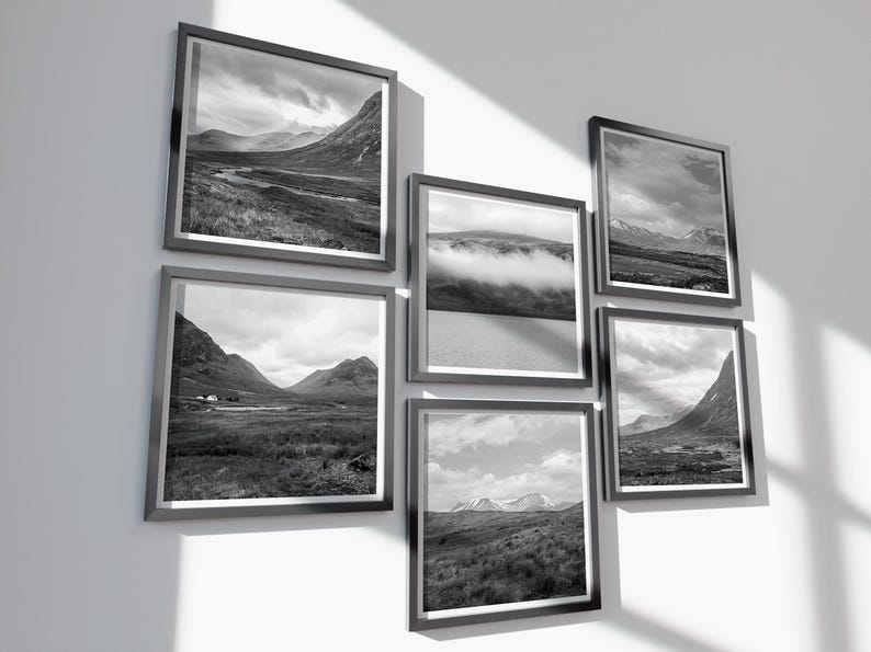 May include: A collection of six framed black and white landscape photographs. The images depict mountain ranges, valleys, and cloudy skies. The frames are dark gray, and the arrangement is displayed on a white wall.