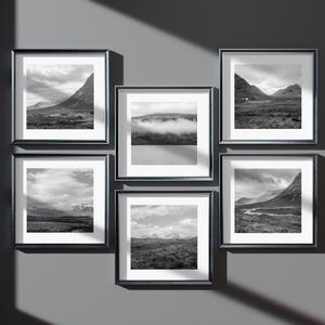 May include: Six framed black and white landscape photographs of mountains, valleys, and cloudy skies are displayed on a gray wall. The frames are square with a white border around the images.