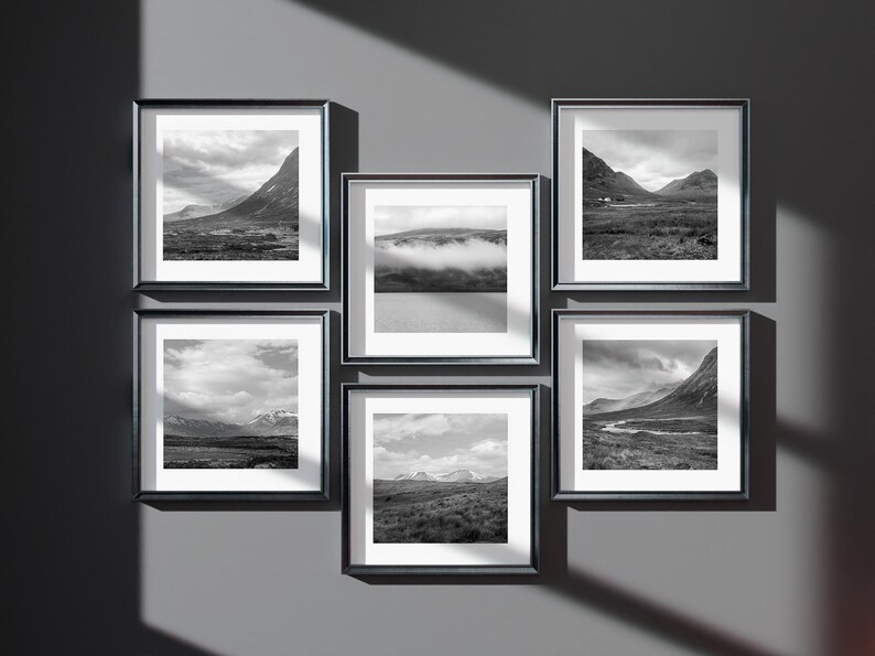 May include: Six framed black and white landscape photographs of mountains, valleys, and cloudy skies are displayed on a gray wall. The frames are square with a white border around the images.