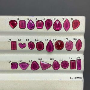 May include: A collection of twenty-four faceted pink gemstones arranged in three rows on a white display tray. Each stone is numbered from 1 to 24, featuring various shapes including pear, oval, rectangular, and heart. The text 10-5mm is visible.