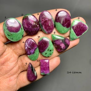 May include: Ten polished ruby zoisite cabochons in various shapes, including ovals, triangles, and a rectangle, featuring deep magenta and vibrant green mineral inclusions. Each stone is numbered from 1 to 10, with a size range of 24-16mm indicated.
