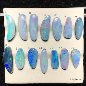 May include: A collection of fourteen oval-shaped opals, each with unique color patterns and iridescence. The opals range in size from 13mm to 9mm. The opals display a variety of colors, including blue, green, and red, with a shimmering effect.