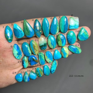 May include: A collection of twenty-nine polished, cabochon-cut gemstones in shades of turquoise, teal, and green, each marked with a small black number from 1 to 29. The stones vary in shape, including ovals, teardrops, and rectangles, with 22-11mm text.