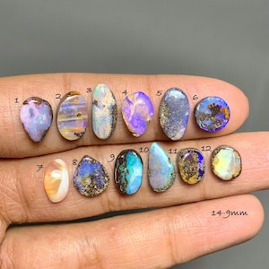 Puede incluir: Doce piedras preciosas de ópalo sueltas dispuestas en dos filas, numeradas del 1 al 12. Cada piedra muestra patrones de colores iridiscentes únicos, incluyendo tonos azules, morados, naranjas y blancos. El texto 14-9mm aparece abajo a la derecha.