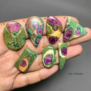 Puede incluir: Siete piedras preciosas cabujón pulidas con una matriz verde e inclusiones magenta incrustadas. Cada piedra está numerada del uno al siete, con formas ovaladas, triangulares e irregulares. El texto indica un rango de tamaño de 31-24mm.