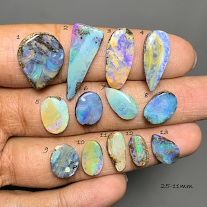 May include: Thirteen polished, multi-colored opals arranged in rows, numbered 1 through 13. Each gemstone displays unique iridescent patterns in shades of blue, green, yellow, and orange. The text 25-11mm is visible in the bottom right corner.