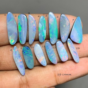 May include: Thirteen elongated, polished opal gemstones with iridescent flashes of blue, green, and pink. Each stone is numbered from 1 to 13, with a size range of 29-14mm printed in the corner. The stones display a milky, translucent base.
