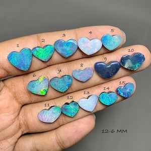 May include: Fifteen heart-shaped opal gemstones arranged in numerical order from 1 to 15. Each stone displays a unique play of color, ranging from vibrant blues and greens to iridescent whites and dark tones. The text 12-6 MM is visible.