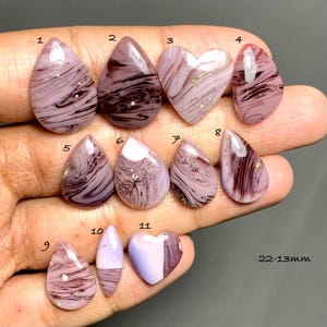 Puede incluir: Once cabujones pulidos de diversas formas, incluyendo gotas, óvalos y corazones, con patrones jaspeados en tonos malva, lavanda y morado oscuro. Las piedras están numeradas del 1 al 11, con texto que indica tamaños de 22-13mm.
