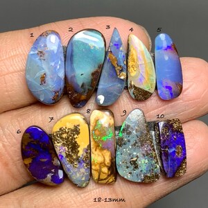 Puede incluir: Una colección de diez piedras preciosas de ópalo pulidas, cada una con patrones y colores únicos. Los ópalos varían en forma y tamaño, con tonos de azul, amarillo, morado y verde. El texto "18-13mm" es visible en la parte inferior de la imagen.