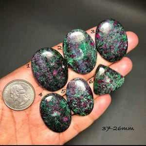 May include: A selection of six ruby-in-zoisite gemstones, displaying a mix of deep red and green colours. The stones are oval and triangular. The size of the stones ranges from 26mm to 37mm.