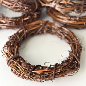 May include: Several rustic brown grapevine wreaths. The wreaths are made of intertwined twigs and vines, creating a natural, circular shape. The wreaths vary in size and are suitable for various decorative purposes.