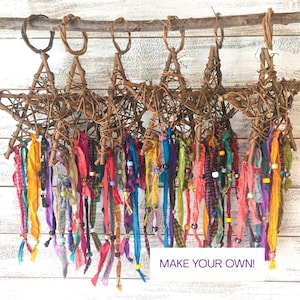 May include: Handmade star-shaped ornaments crafted from woven twigs, suspended from a branch. Each star features colorful fabric ribbons in various hues, accented with beads. The text "MAKE YOUR OWN!" is visible.