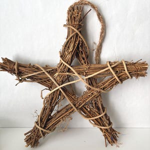 May include: A rustic, five-pointed star decoration crafted from natural twigs and vines. The star is a warm brown color, with lighter-colored vines wrapped around the points and a jute loop for hanging. This decorative star is perfect for adding a touch of nature to any space.