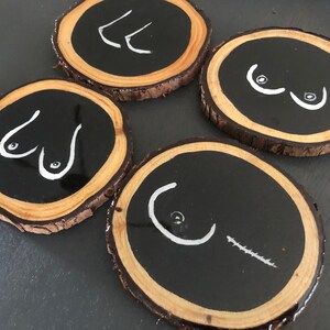 May include: Four round wooden coasters with black painted centres and white painted abstract designs. The coasters are made from natural wood with a rough bark edge.