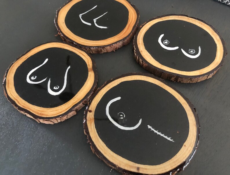May include: Four round wooden coasters with black painted centres and white painted abstract designs. The coasters are made from natural wood with a rough bark edge.