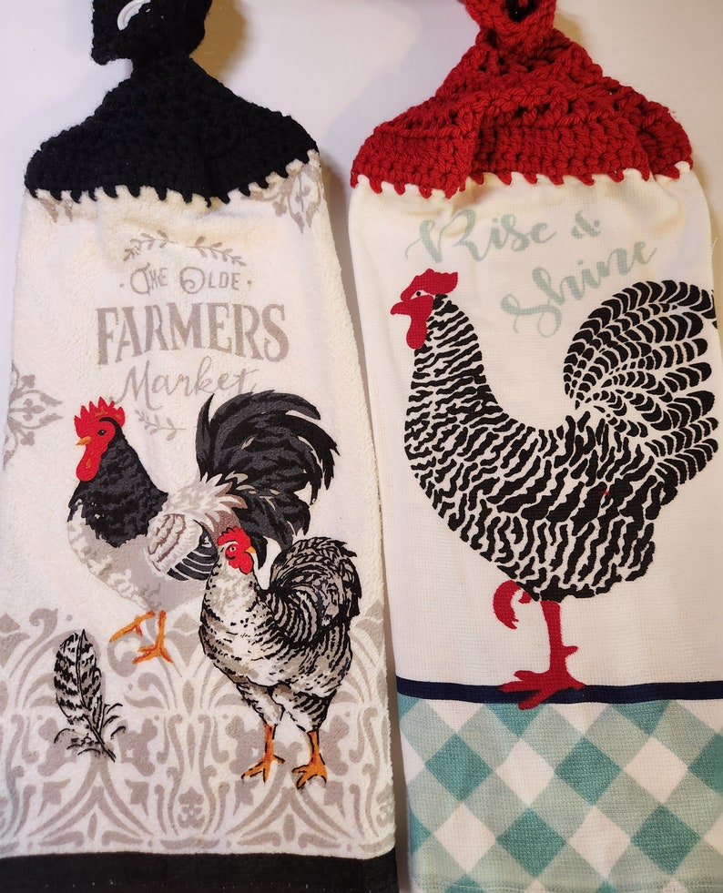 May include: Two kitchen towels with rooster designs. One towel has a black crocheted hanging loop and says "The Olde Farmers Market". The other towel has a red crocheted hanging loop and says "Rise & Shine".