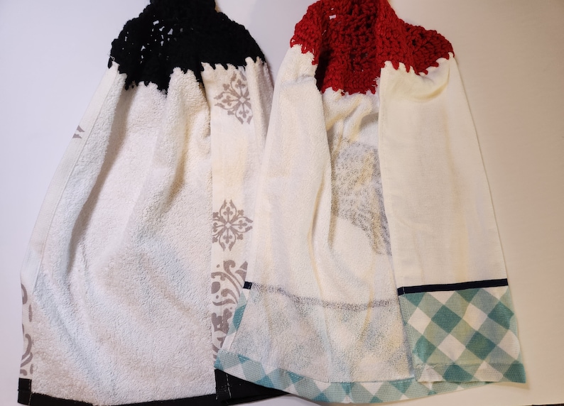 May include: Two white kitchen towels with a crocheted top. One towel has a black crocheted top and the other has a red crocheted top. Both towels have a patterned design and a plaid trim.