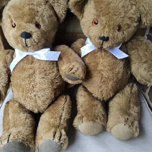 May include: Two brown teddy bears with white bows with blue polka dots. The bears are sitting on a white surface.