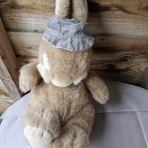 May include: A plush bunny rabbit with soft, brown fur and a gray hat. The bunny has long ears and white accents on its chest and feet. The toy is sitting on a light gray surface.