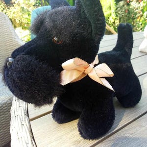 May include: Black plush toy dog with a pink bow. The dog is sitting on a wooden surface.