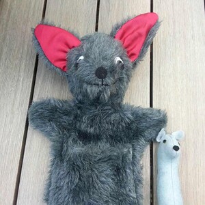 Op de afbeelding: Een grijze, harige pop met rode oren en een kleine grijze pop met een zwarte neus. De poppen staan op een houten oppervlak.