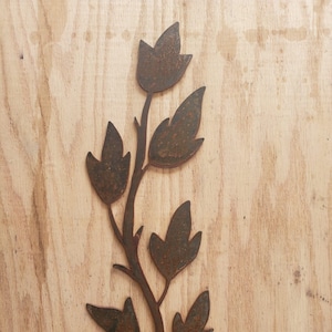 May include: A rusty metal wall decor in the shape of a stylized branch with leaves. The branch is brown and the leaves are a darker brown.