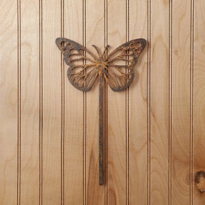 Peut inclure: Un piquet de jardin en métal rouillé en forme de papillon avec un motif découpé décoratif. Le piquet est brun et a un aspect rustique.