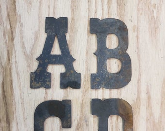 May include: Four metal letters, A, B, C, and D, with a rustic, distressed finish. The letters are cut out in a decorative, western-style font.