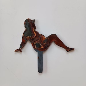 May include: A rusty metal silhouette of a person sitting with their legs outstretched. The silhouette is attached to a metal rod.