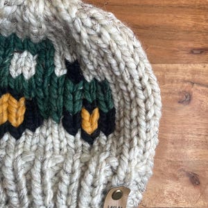May include: A chunky knit beanie in cream, green, black, and yellow. The hat features a geometric design and a small leather tag with the initials "WW". The beanie is made of thick yarn, perfect for cold weather.