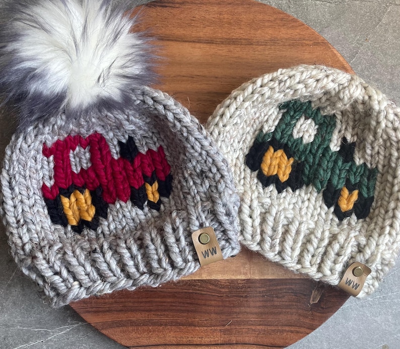 May include: Two knitted beanies with truck designs. One is gray with a red truck, the other is off-white with a green truck. Both have black and yellow accents, and a leather tag with "WW". The gray beanie has a fluffy gray pom-pom.