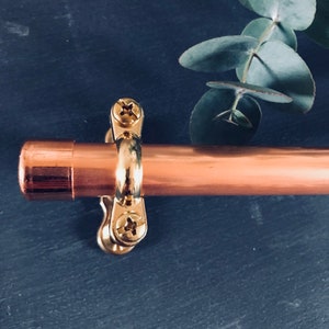 May include: A copper pipe with a gold metal bracket and screws. The bracket is attached to the pipe with two screws. The pipe is on a dark blue background.