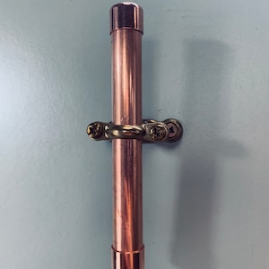 Könnte beinhalten: Ein Türgriff aus Kupferrohr mit einer Messinghalterung. Der Griff ist an beiden Enden mit einer Kupferkappe versehen.