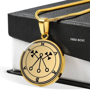 May include: Gold pendant necklace with a black sigil featuring a symbol with three circles and two crossed axes. The pendant is round and has a black border with letters around the edge. The necklace is on a black box with the words "FREE BOX!" printed on it.