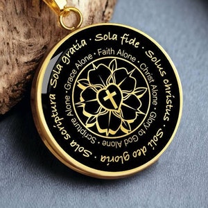 Puede incluir: Un collar de oro con un colgante negro que presenta una flor estilizada con una cruz en el centro. El colgante tiene el texto "Sola Scriptura Sola Gratia Sola Fide Solus Christus Gloria Deo Soli" inscrito alrededor del borde.