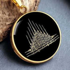 Puede incluir: Un collar de cadena dorada con un colgante redondo negro que presenta un diseño dorado de un templo con detalles intrincados.