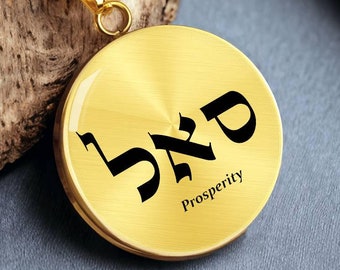 Puede incluir: Collar de oro con un colgante redondo que presenta la palabra hebrea para la prosperidad, "Shefa", en letras negras. El colgante también tiene la palabra "Prosperity" escrita en inglés debajo de la palabra hebrea.