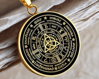 May include: Gold-colored pendant necklace with a circular pendant featuring a black background and gold-colored text and symbols. The pendant has a Celtic knot design in the center and is inscribed with astrological and seasonal references. The chain is a gold-colored snake chain.