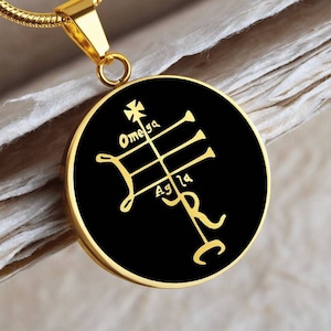 May include: Gold chain necklace with a black circular pendant featuring a gold symbol and the words "Omega" and "Agla" in a stylized font.