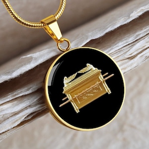 May include: A gold necklace with a round pendant featuring a black background and a gold image of the Ark of the Covenant.