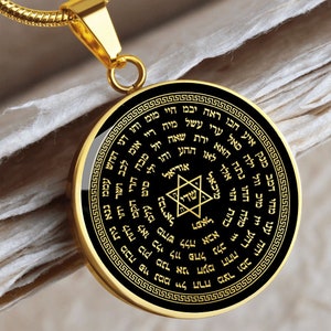 May include: A gold pendant necklace with a black circular charm featuring a Star of David and Hebrew text. The charm is surrounded by a decorative border.