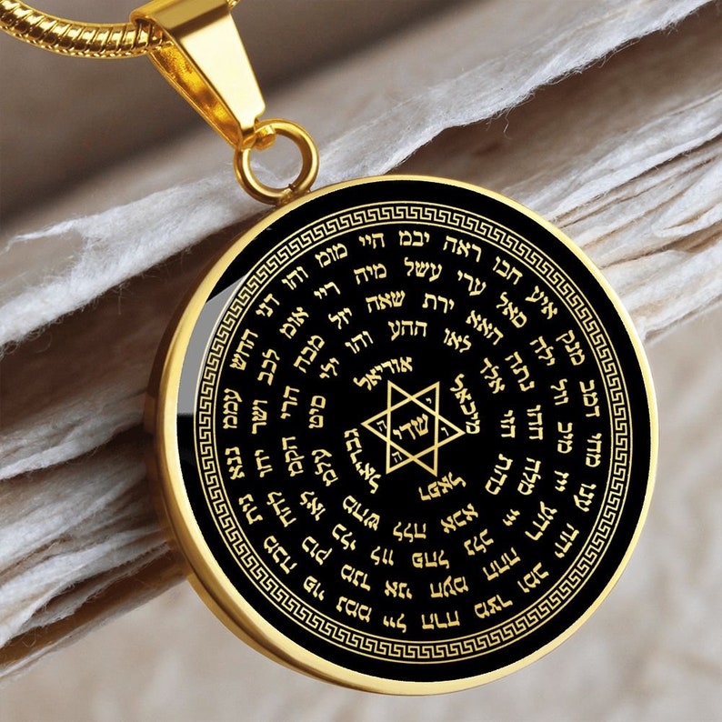 May include: A gold pendant necklace with a black circular charm featuring a Star of David and Hebrew text. The charm is surrounded by a decorative border.